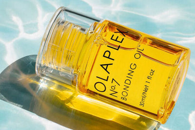Elegant beholder med honningfarvet olie. Olaplex No.7 Bonding Oil. Swimmingpool baggrund.